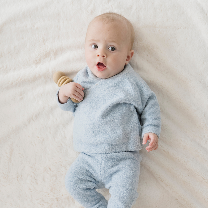 Baby in a light blue outfit lying on a white blanket
