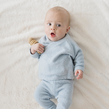 Baby in a light blue outfit lying on a white blanket