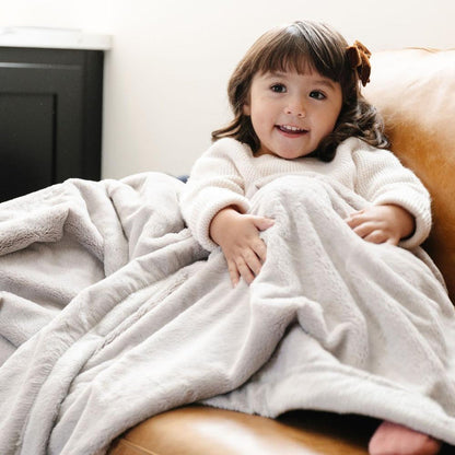 A little girl is wrapped in a Luxury Toddler Feather (light gray) Colored Lush Saranoni Blanket. The soft blanket is a baby blanket or toddler blanket.