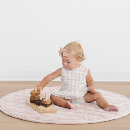 Baby girl sits on a pink minky play mat with some toys.