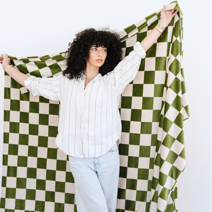 Woman stands holding a Olive and Cream checkered minky stretch XL blanket.