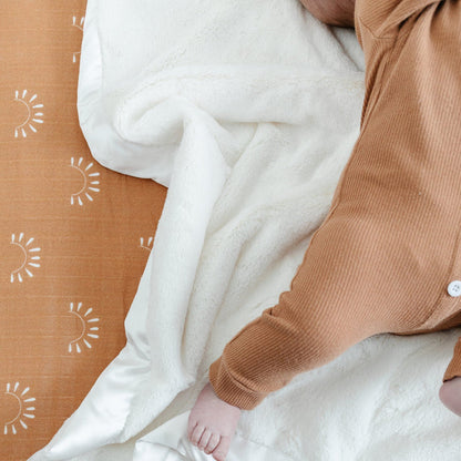 Baby laying in crib with a luxuriously soft white mini satin bordered blanket.