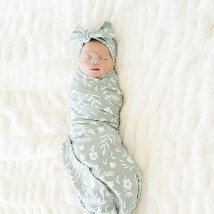 Baby girl swaddled in Saranoni Sweet Alyssum Stretchy Swaddle with a matching bow.