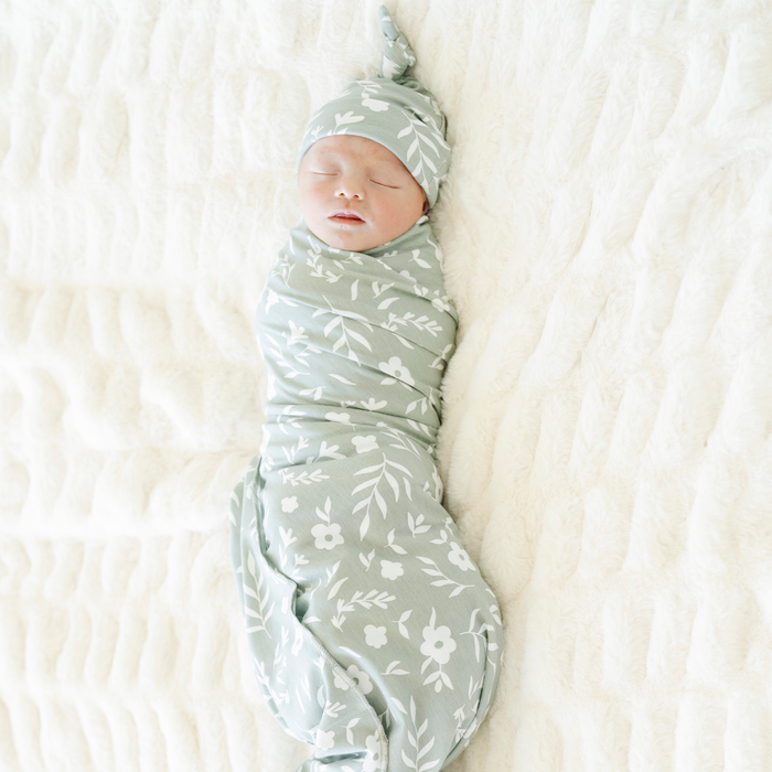 Baby girl swaddled in Sweet Alyssum Saranoni Stretchy Swaddle with a matching hat.