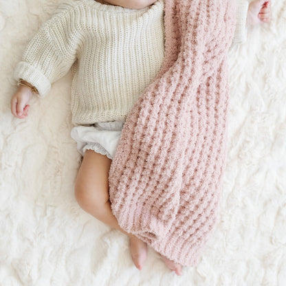 Baby girl sleeping in crib with link waffle knit blanket.