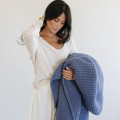 Person holding a folded, blue waffle knit throw blanket.